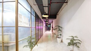 A corridor with potted plants, a tiled floor, and a glass wall with papers on it. - Hotel The Rasa Kanti Nagar  (New Delhi)