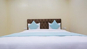 A neatly made bed with a tufted headboard, white bedding, and two light blue pillows. - Hotel Mannat bhera enclave (New Delhi)