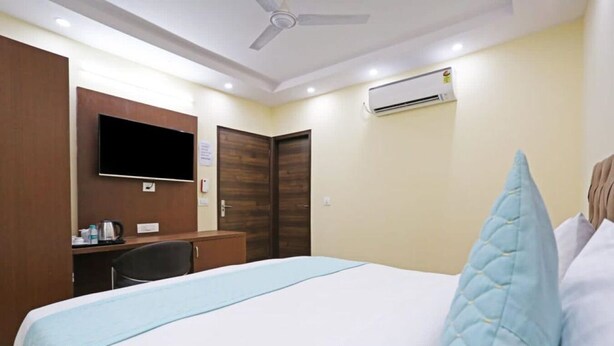 A hotel room with a bed, a desk, a television, and an air conditioning unit. - Hotel Mannat bhera enclave (New Delhi)