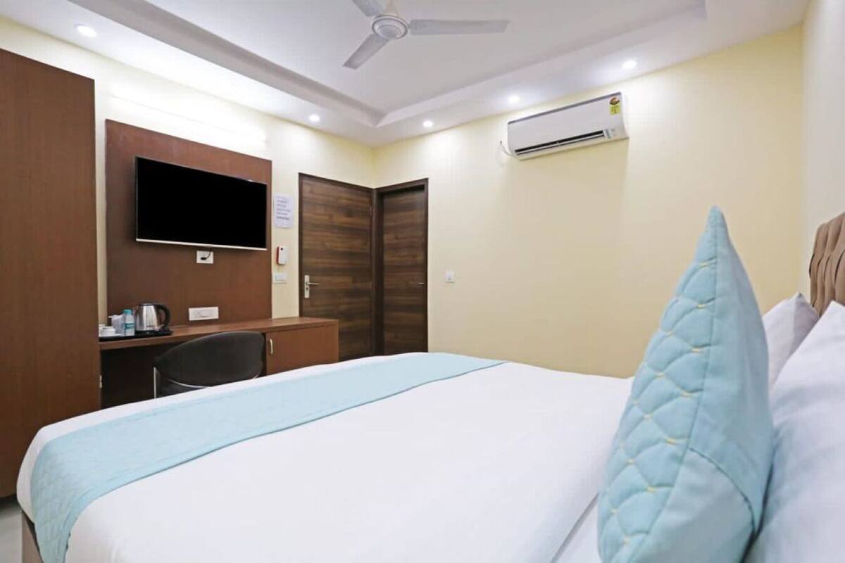 A hotel room with a bed, a desk, a television, and an air conditioning unit.