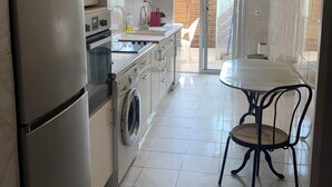 A modern kitchen with a refrigerator, microwave, oven, and washing machine. There is a dining area with a table and chairs. - Grand T3 Terrasses Jardin (Antibes)