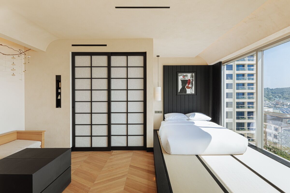 A modern hotel room with a large bed, a wooden floor, a sliding shoji screen door, and a city view.
