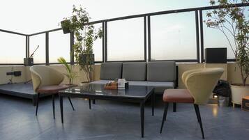 A rooftop terrace with a sofa, two armchairs, a coffee table, and potted plants.