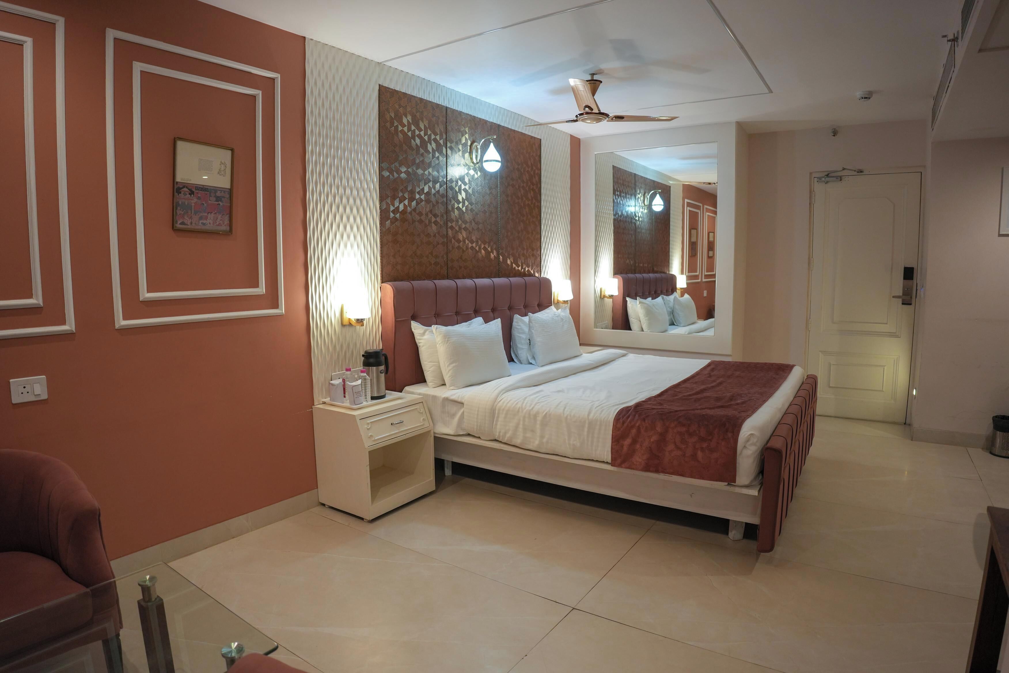 Une chambre d’hôtel avec un grand lit, une table de chevet, un miroir et un ventilateur de plafond.