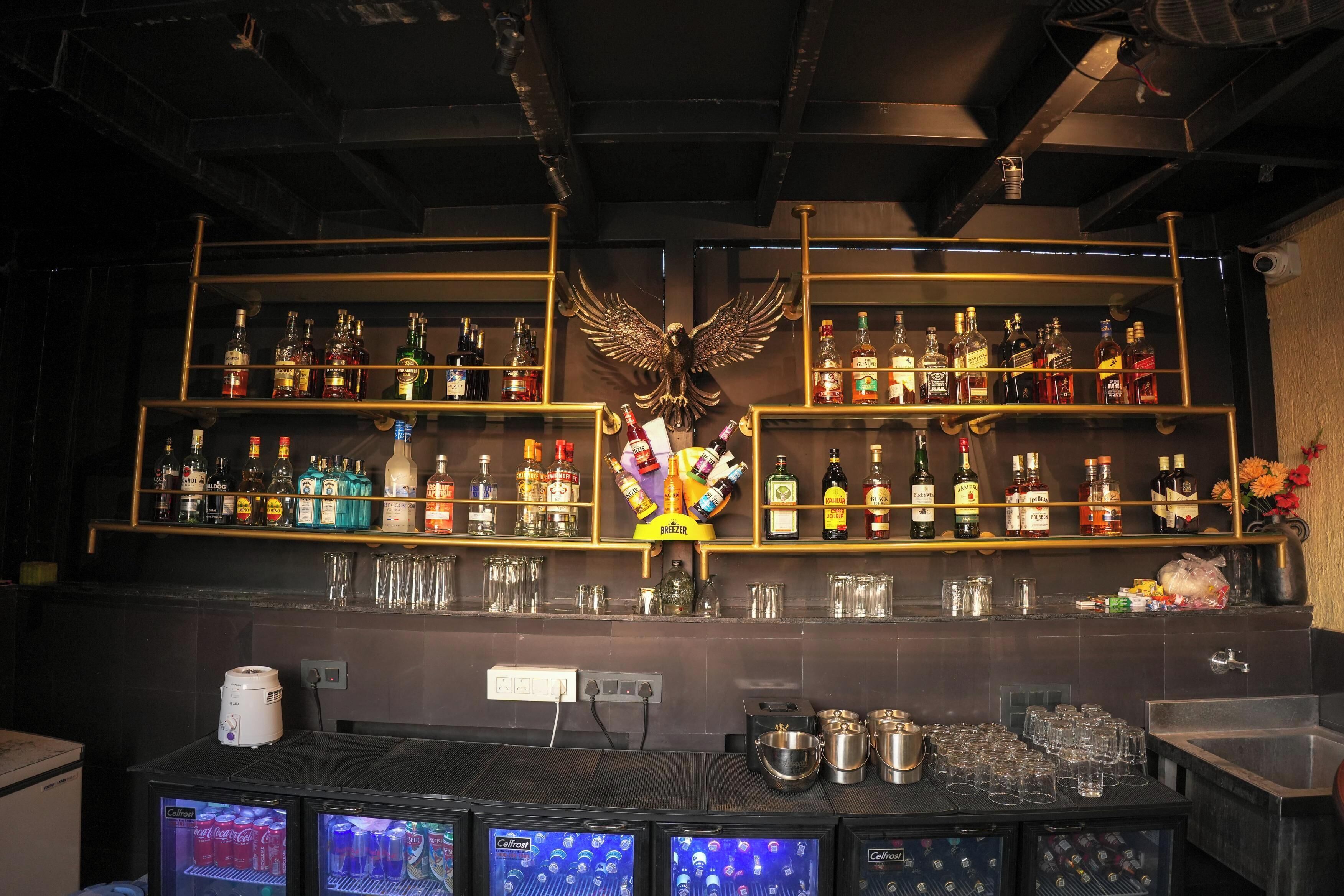 A bar area with shelves of liquor bottles, a decorative eagle, and a refrigerator with beverages.