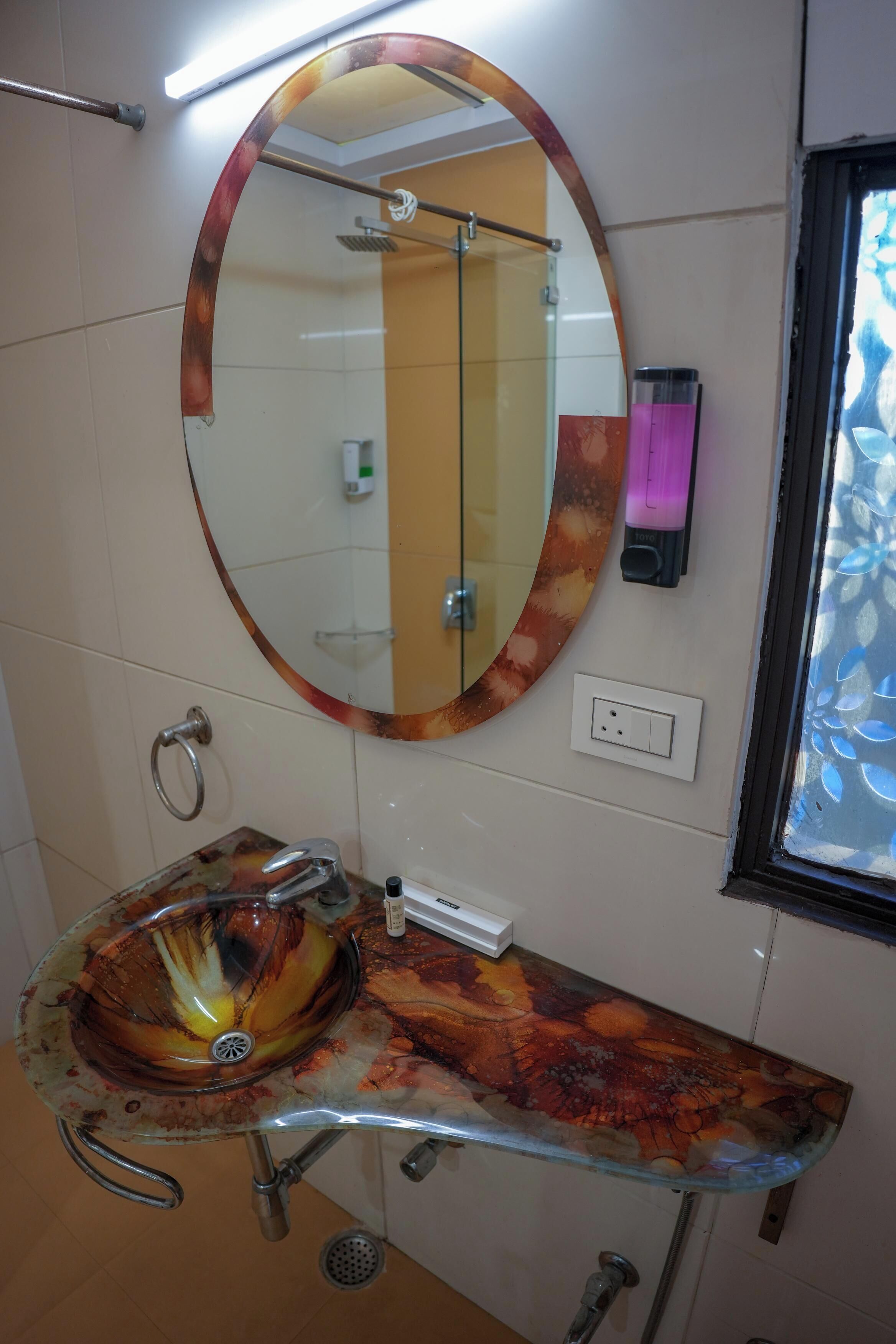 Een badkamer met een ronde spiegel, een glazen wastafel en een douche.