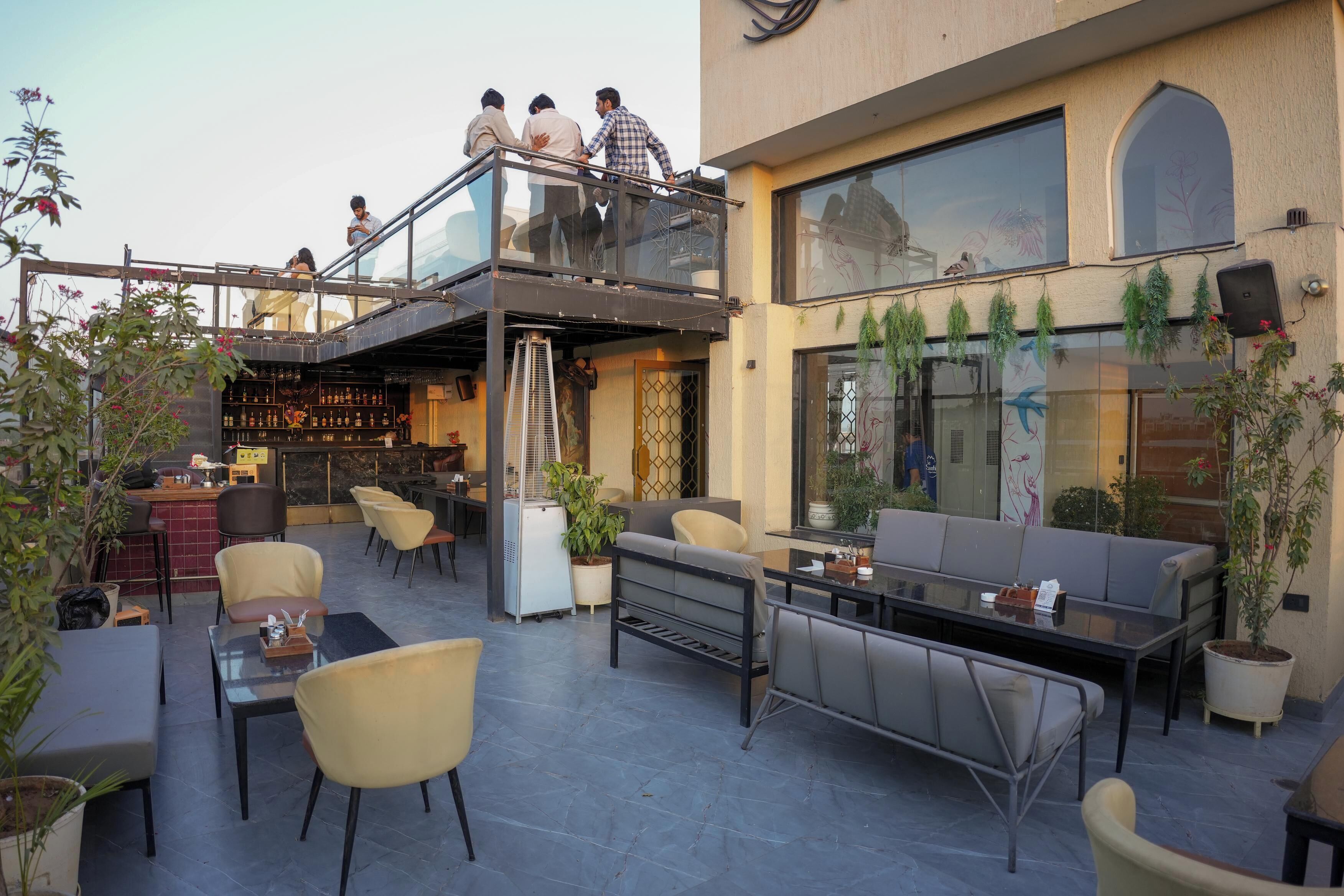 An outdoor seating area with tables and chairs, a bar, and a glass railing overlooking the space.
