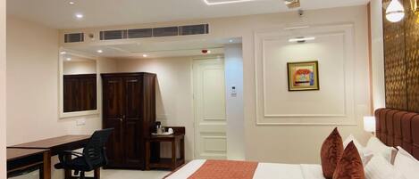 A hotel room with a bed, desk, chair, wardrobe, and ceiling fan.