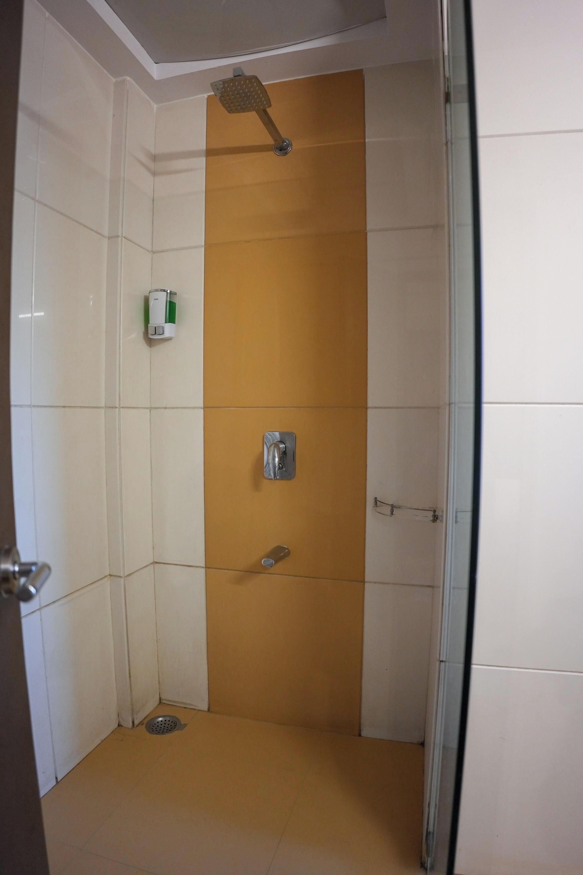 Um chuveiro pequeno e fechado, com uma parede amarela de destaque, um chuveiro manual, um dispensador de sabonete e uma torneira manual.
