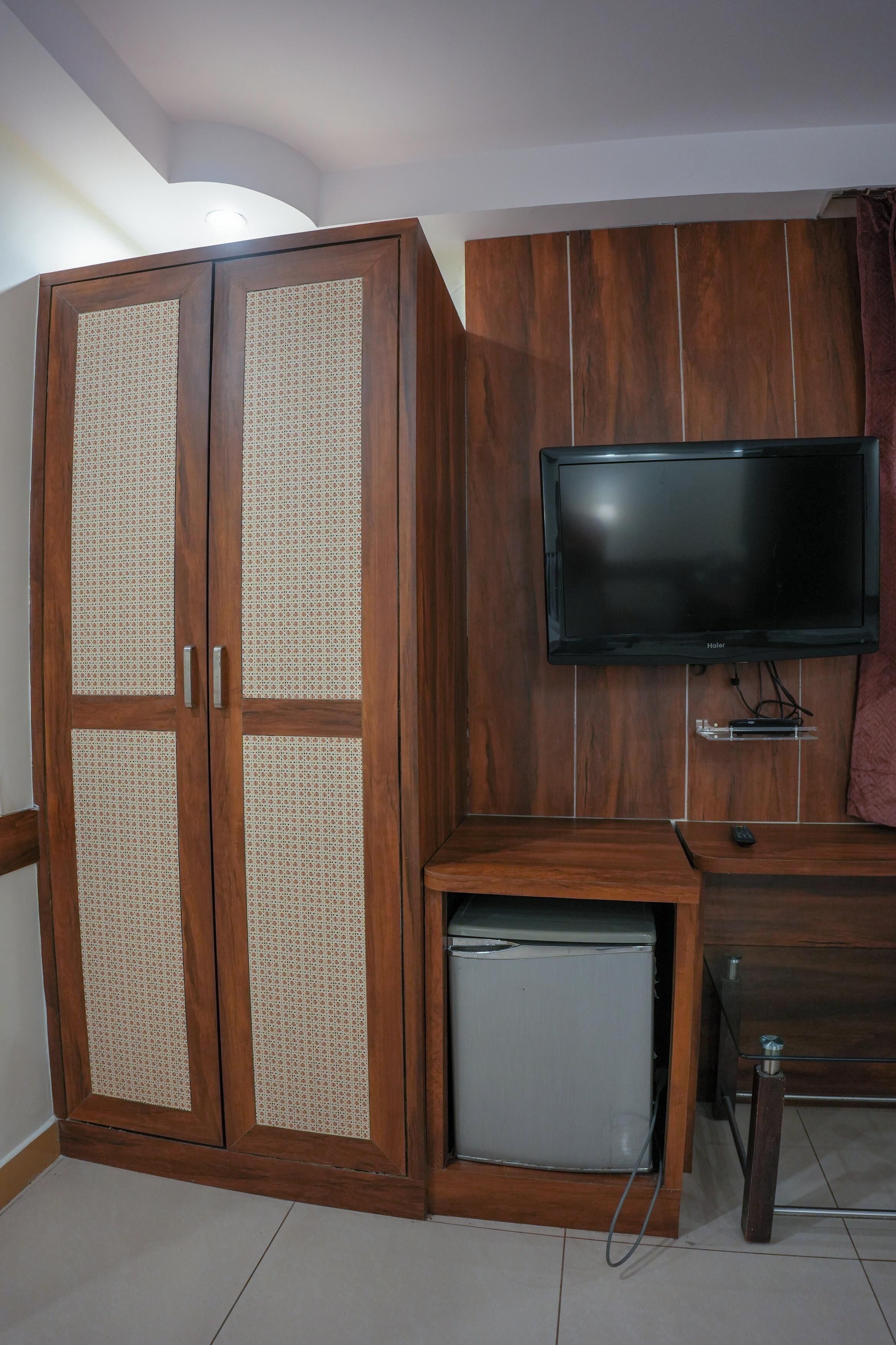 Quarto com guarda-roupa de madeira, televisão na parede e um frigorífico pequeno.