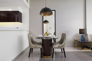 A modern dining area with a round table, two chairs, a decorative pendant light, and a side table with a lamp. - Maison Privee - Splendid Apt w/ Large Balcony in Business Bay (Dubai)