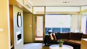 A modern living room with a large window, a sofa, a coffee table, and a fireplace. - Hepburn Hideaway~ large Villa ~ Hepburn~Daylesford
 (Hepburn Springs)