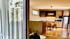 A modern living room with a sofa, a coffee table, and a dining area with a table and chairs. There is a kitchen area with cabinets and appliances in the background. - Hepburn Hideaway~ large Villa ~ Hepburn~Daylesford
 (Hepburn Springs)