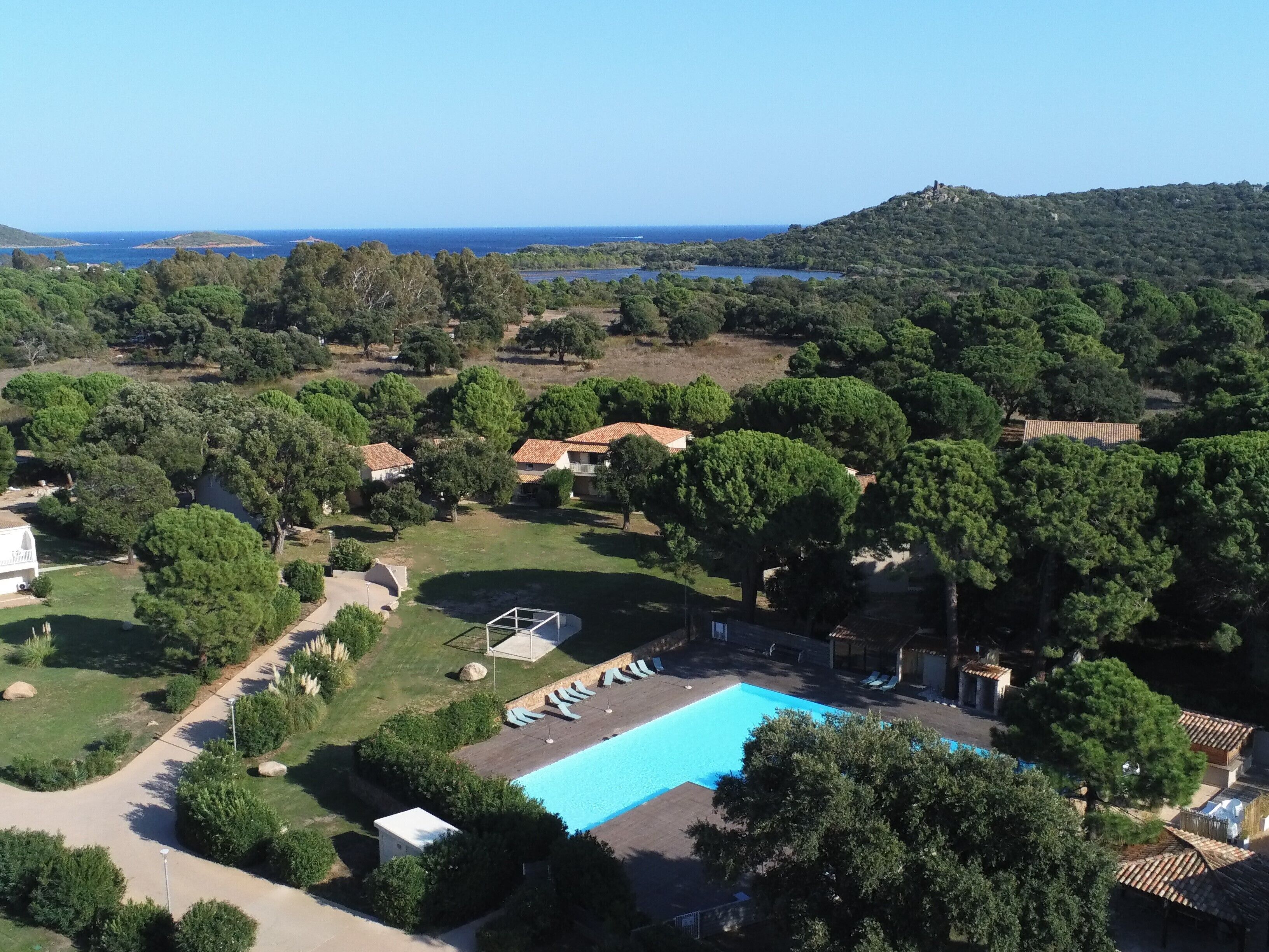 Ett semesterhotell med en swimmingpool, omgivet av frodig grönska och med utsikt över havet.