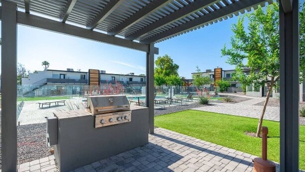 An outdoor patio with a barbecue grill, seating area, and a view of a pool and buildings in the background. - King Bed, Pool, Parking, Theme Park, Gym SOON! (Phoenix)