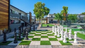 A courtyard with a chessboard setup, surrounded by buildings with balconies and a clear sky. - King Bed, Pool, Parking, Theme Park, Gym SOON! (Phoenix)