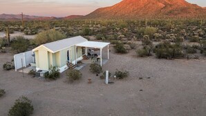 A single-story building with a covered patio area, surrounded by desert vegetation and a prominent mountain in the background. - Saguaro Sunset Oasis (Tucson)