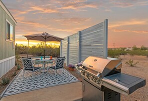 Un patio exterior con una parrilla, una mesa con sillas y una alfombra estampada.