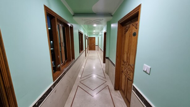 A hallway with a marble floor, wooden doors, and a ceiling with a central light fixture. - Hotel Apsara By Royal Collection Hotels (Dehradun)