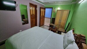 A bedroom with a bed, a wooden wardrobe, a mirror, and a green wall. - Hotel Apsara By Royal Collection Hotels (Dehradun)