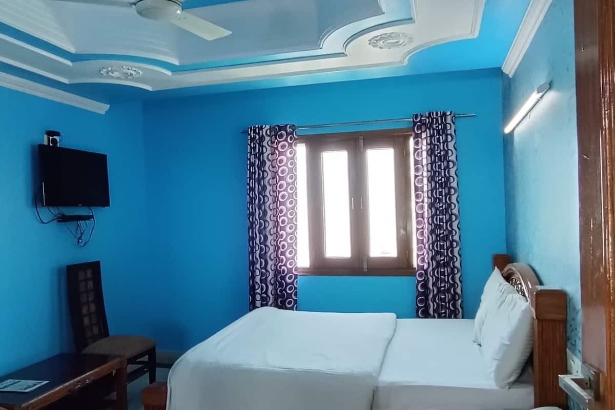 A bedroom with a bed, a ceiling fan, a TV, and a window with curtains.