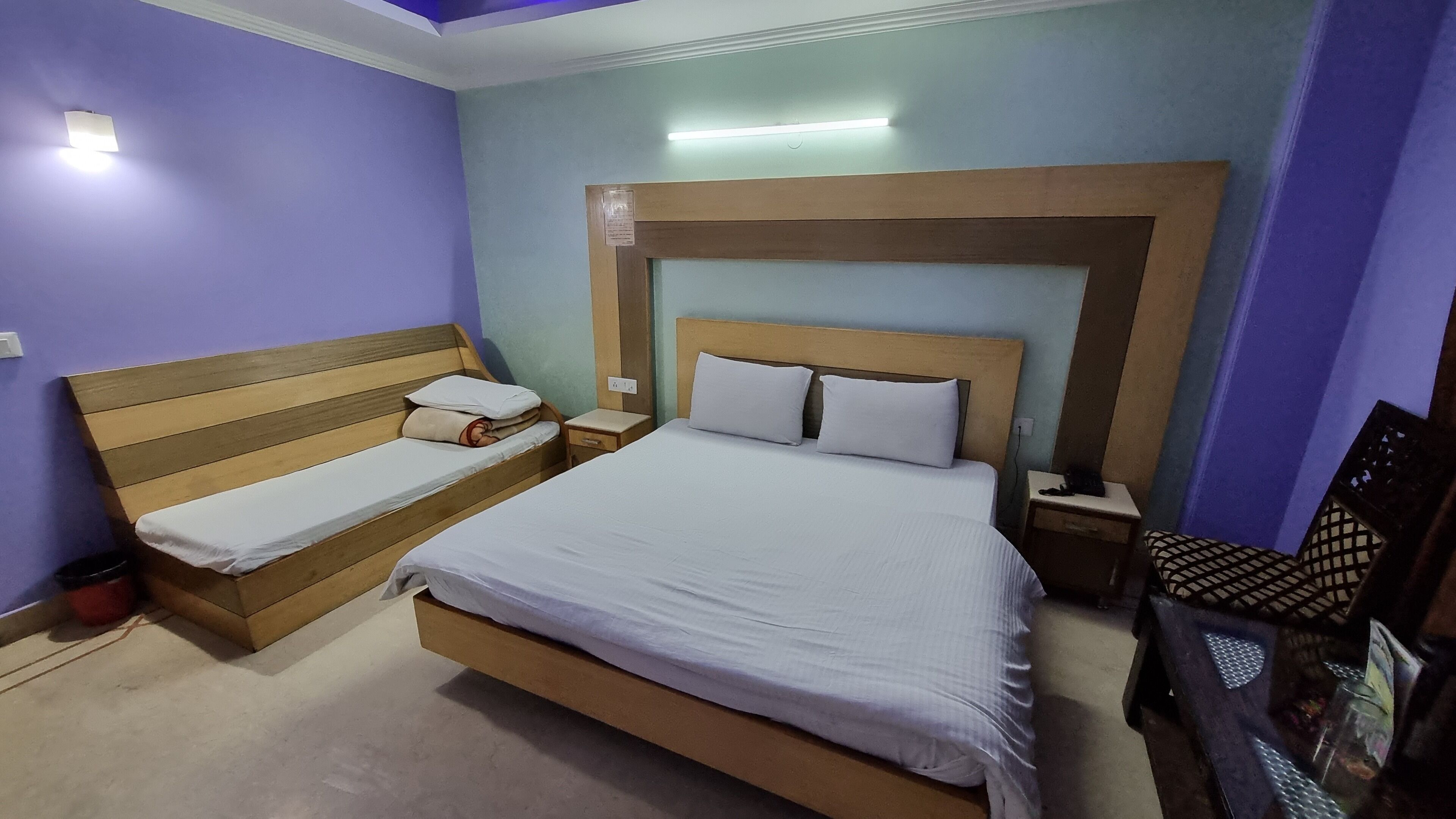 A bedroom with a large bed, a smaller bed, wooden headboards, and a nightstand with a lamp.