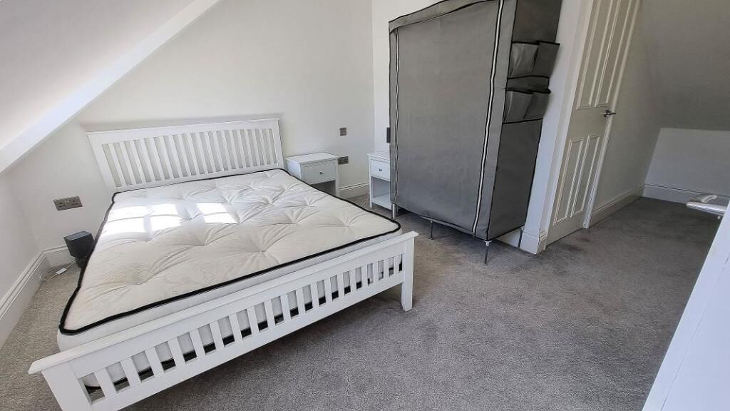 A bedroom with a white bed, a wardrobe, and a small bedside table.