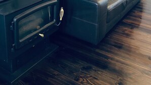 A black leather sofa against a grey wall with a black wood-burning stove.