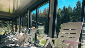 Un espacio de descanso al aire libre con sillones y mesas modernos, grandes ventanales con vistas a una zona boscosa.