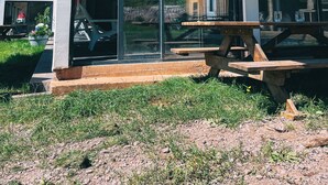 Un edificio moderno con amplios ventanales de vidrio, una terraza de madera y una mesa de picnic.