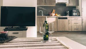 Una cocina moderna con armarios de madera, horno empotrado y microondas. Hay una mesa de comedor con una botella de vino y dos copas. Un televisor está sobre un mueble frente a la cocina.