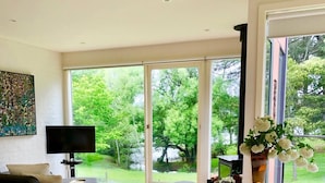 A modern living room with a glass dining table, a black sofa, and a TV. - Lake Daylesford Villa 2~ lake frontage large villa
 (Daylesford)