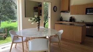 A modern kitchen with a round glass table and white chairs, wooden cabinets, and a view of the garden. - Lake Daylesford Villa 2~ lake frontage large villa
 (Daylesford)