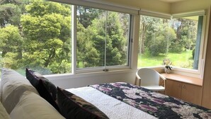 A bedroom with a large window, a bed with a floral bedspread, a chair, and a desk with a vase. - Lake Daylesford Villa 2~ lake frontage large villa
 (Daylesford)