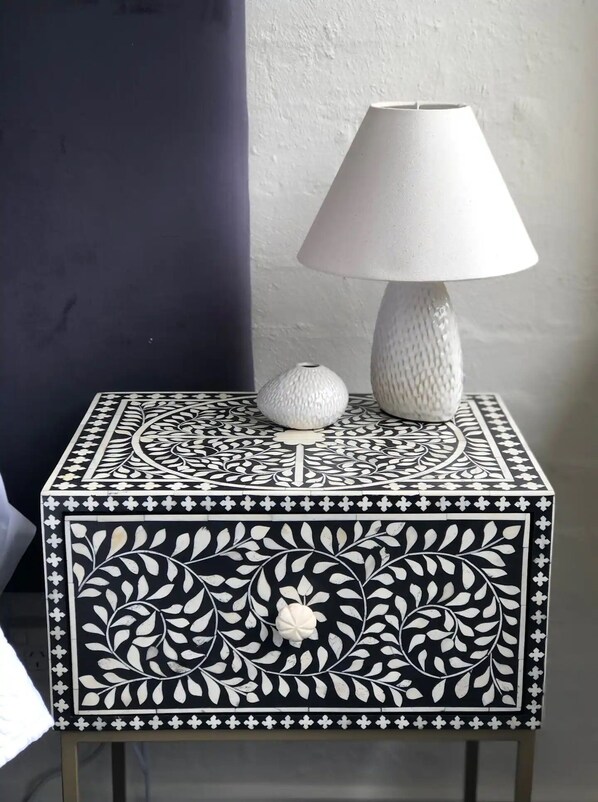 Una mesita auxiliar pequeña, cuadrada, con estampado blanco y negro, con una lámpara y un objeto decorativo encima.