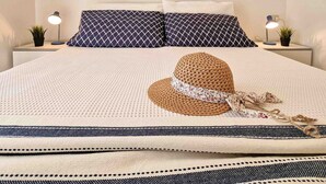 A neatly made bed with patterned pillows, a woven hat, and a decorative mirror on the wall. - Comfortable Apartment Close to Bibione sea (San Michele al Tagliamento)