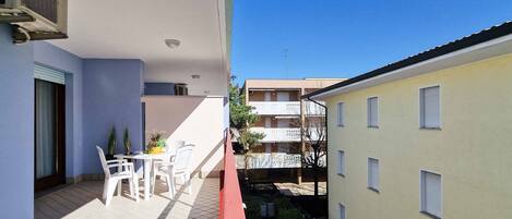 A balcony with a table and chairs, a red railing, and a view of adjacent buildings.