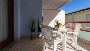 A balcony with a table and chairs, potted plants, and a view of a building. - Comfortable Apartment Close to Bibione sea (San Michele al Tagliamento)