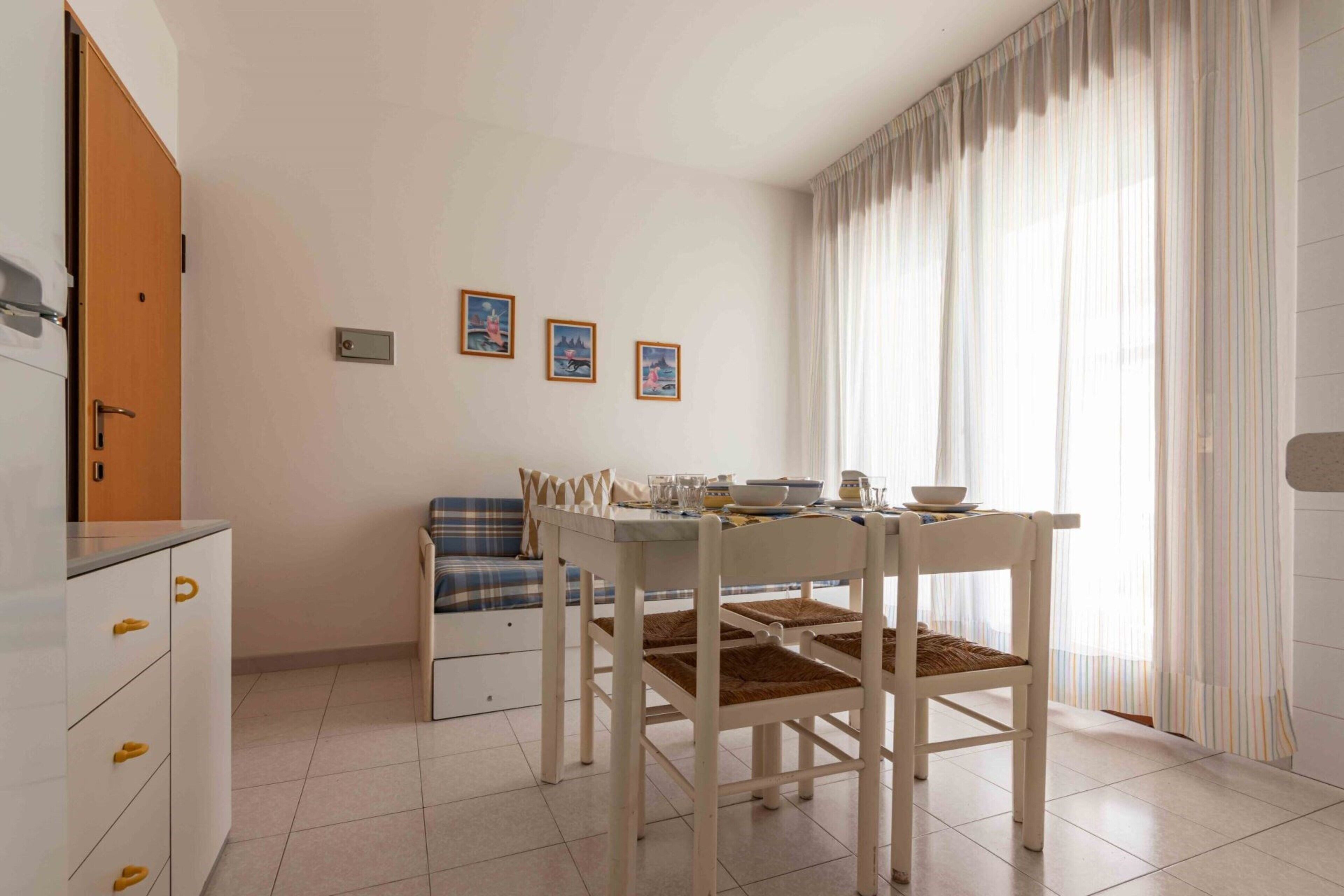 Un espace de vie compact comprenant un coin cuisine, un coin repas avec une table et des chaises, un canapé et une fenêtre avec des rideaux.