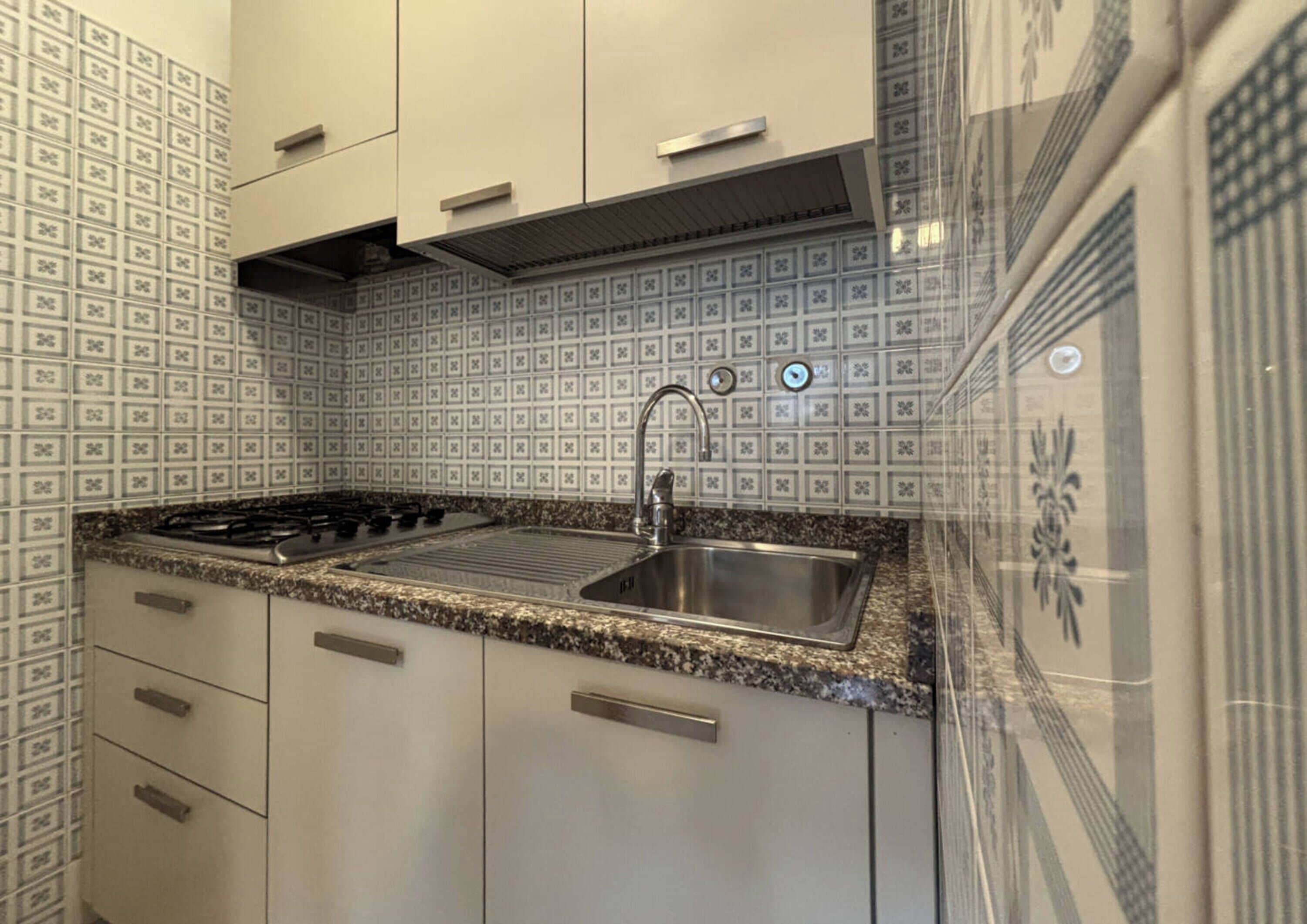 Cocina con encimera de granito, pileta de acero inoxidable y armarios blancos.
