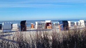 Sillas de playa numeradas 358, 365 y 356 alineadas en una playa arenosa, con vista despejada al océano y montañas distantes.