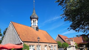 Un pueblo europeo tradicional con un campanario de iglesia destacado, calles adoquinadas y un edificio de ladrillo rojo con un reloj.