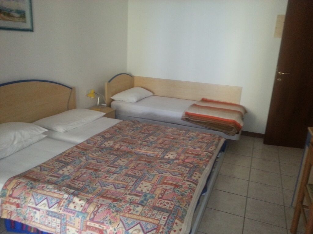 Un dormitorio con dos camas, cabeceros de madera, una mesita de noche con lámpara y una puerta a la derecha.
