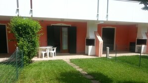 A building with a red facade, multiple doors, and a small grassy area with a fence and chairs. - Apartment With Shared Pool for 4 Guests (San Michele al Tagliamento)