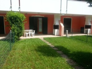 Un edificio con fachada roja, una pequeña zona verde y una cerca blanca.