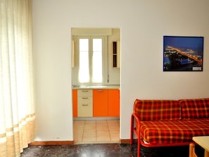 Une pièce avec un coin cuisine, un canapé rouge à carreaux et une affiche représentant un paysage urbain accrochée au mur.