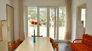 Un comedor con mesa y sillas, un sofá, y vistas al exterior a través de amplios ventanales.