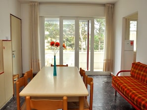 Ein Essbereich mit Tisch, Stühlen, einer Blumenvase, einer Couch und einer Schiebetür zu einem Außenbereich.
