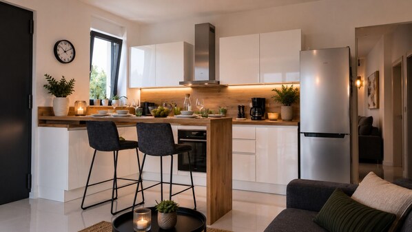 A modern kitchen with white cabinets, a stainless steel refrigerator, and a wooden island with bar stools.
