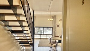 A staircase with a black railing leading to a dining area with a table and chairs. - Kubler's House-  By Beach Apartments TLV (Tel Aviv)